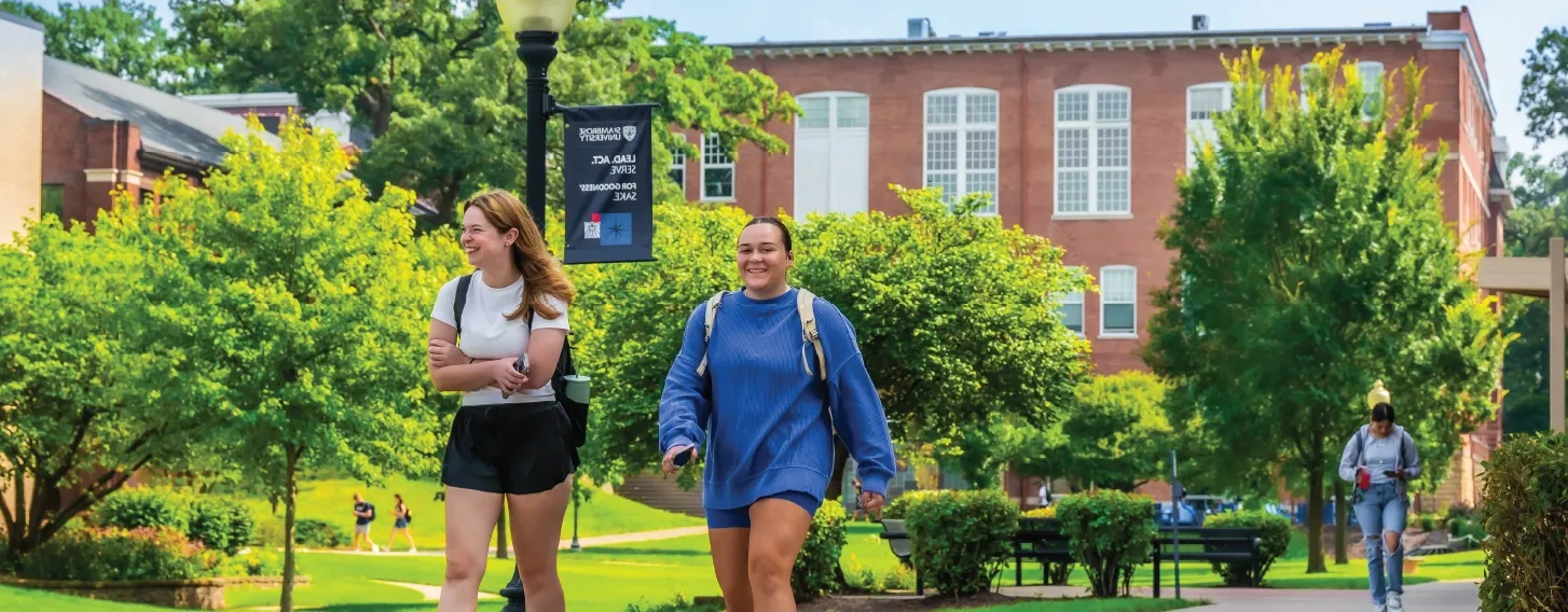 Two students walking across campus, smiling.